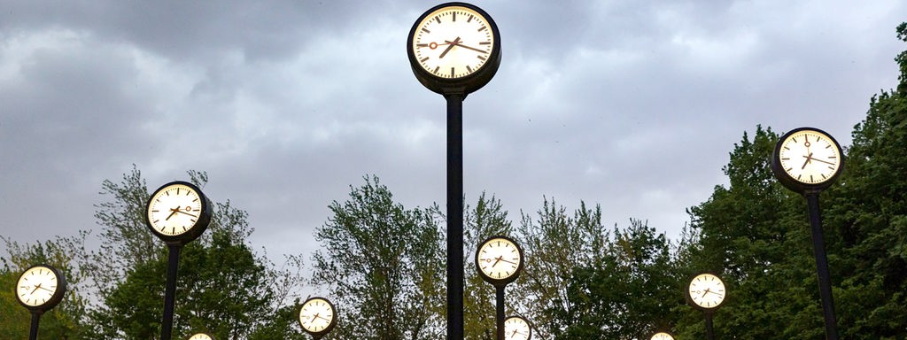 Mehrere Uhren der Installation 'Zeitfeld' von Klaus Rinke vor verdunkeltem Himmel.